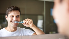man smiling in the mirror while cleaning his teeth after following a guide to tooth brushing